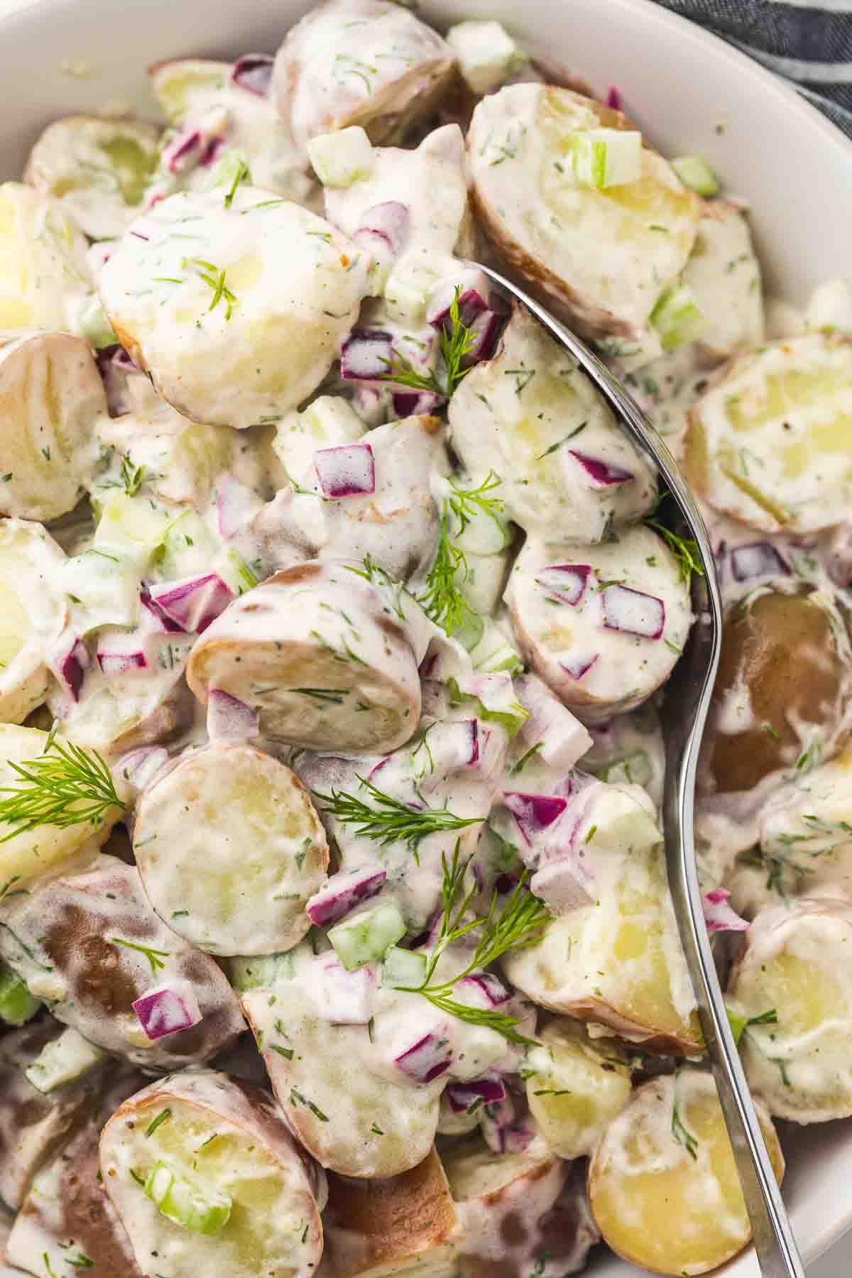 Overhead shot of red potato salad served in a white serving bowl with a serving spoon.