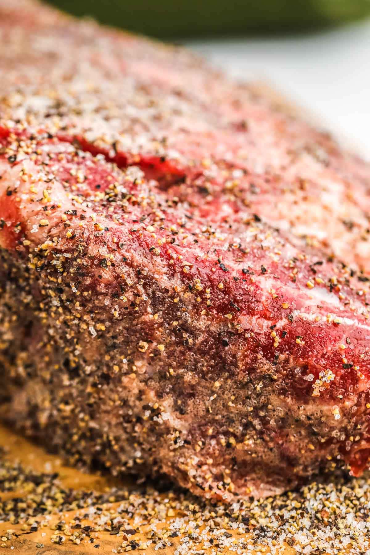 Raw cut of beef chuck generously seasoned with salt and coarsely ground black pepper