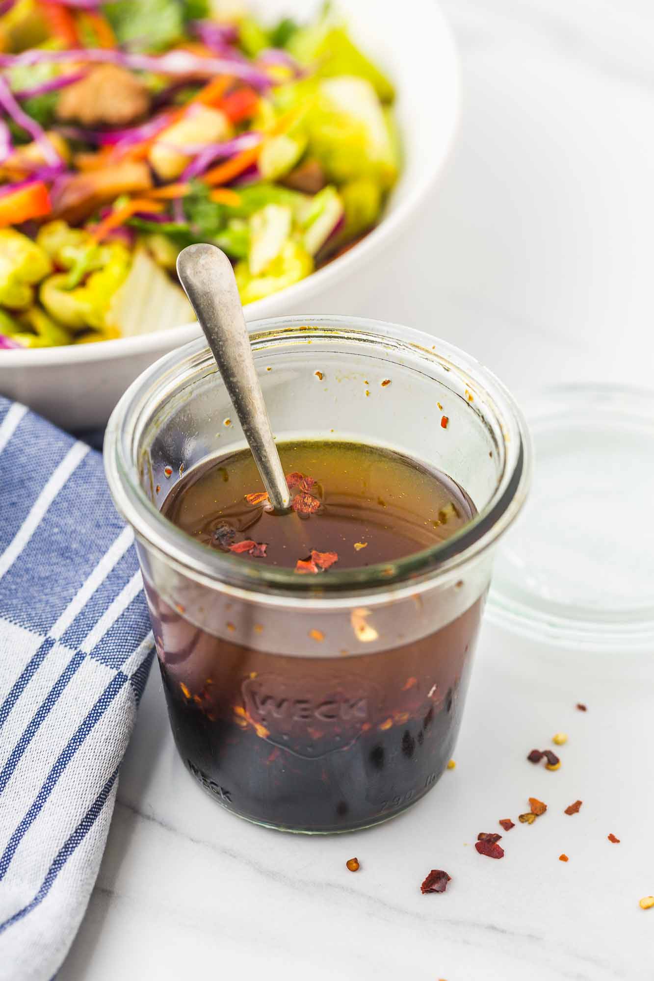 Soy based dressing in a weck jar with a spoon, and a salad in the background