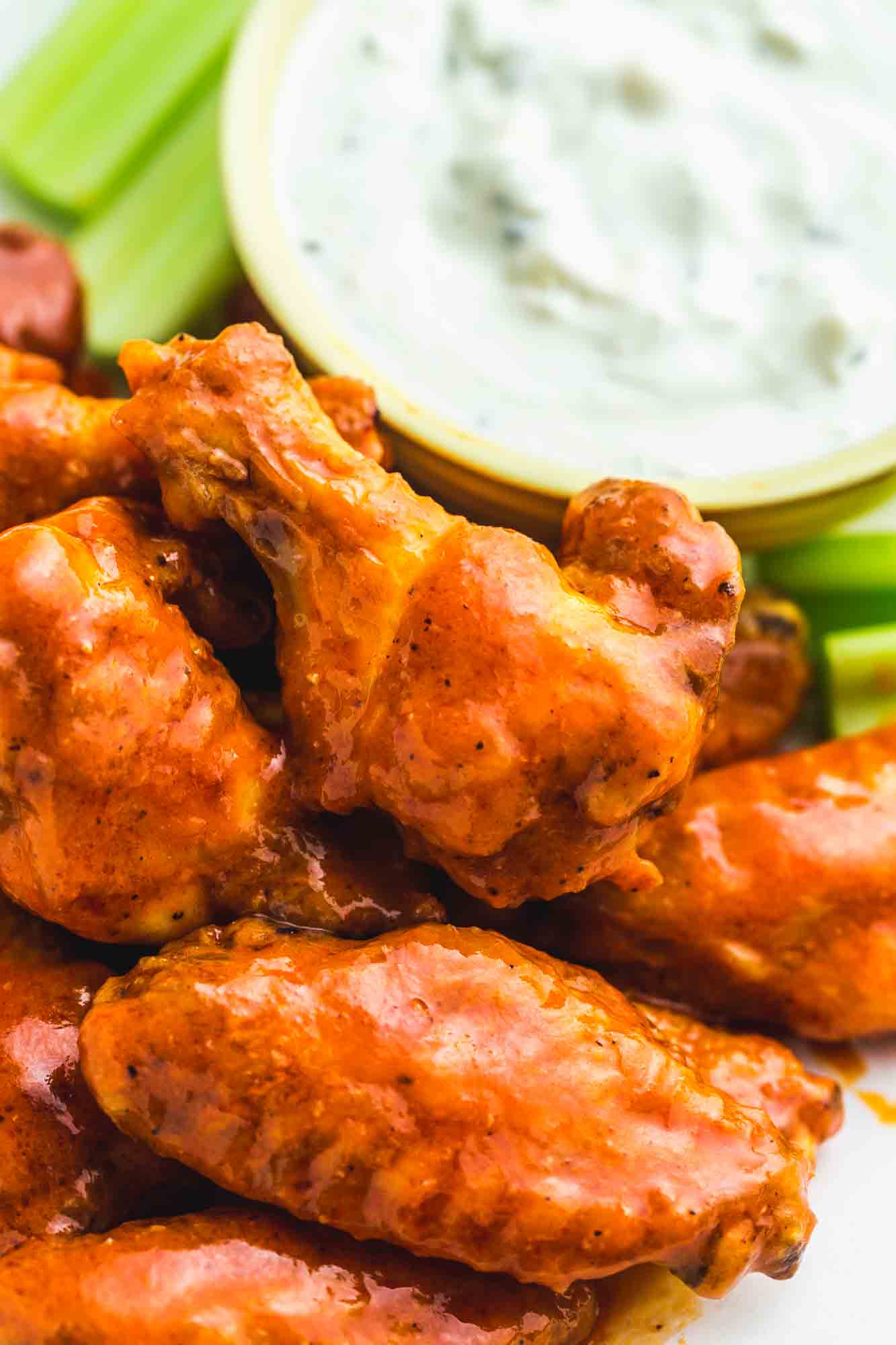 Buffalo chicken wings stacked, with blue cheese dip and celery sticks in the background.