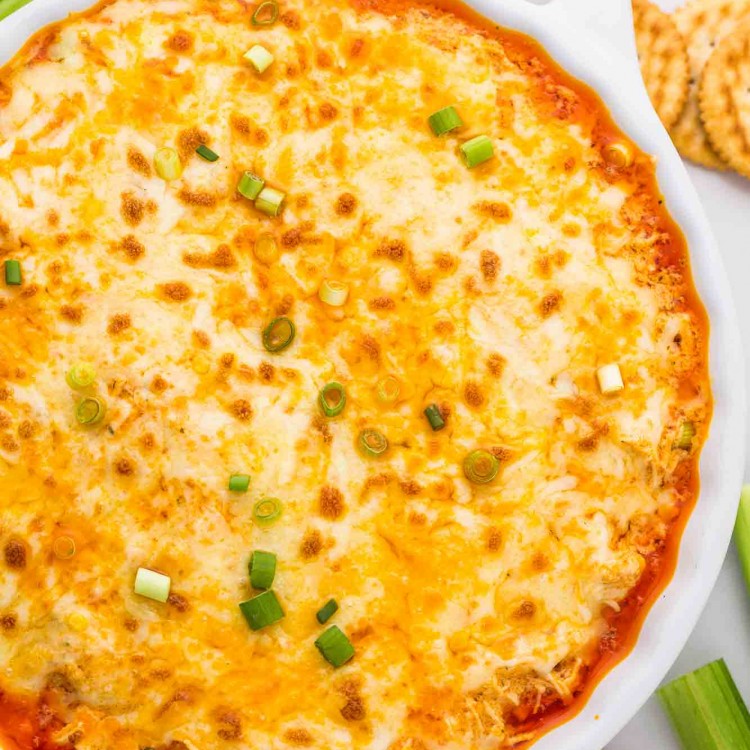 Hot buffalo chicken dip in a baking dish, with celery sticks and Ritz crackers.
