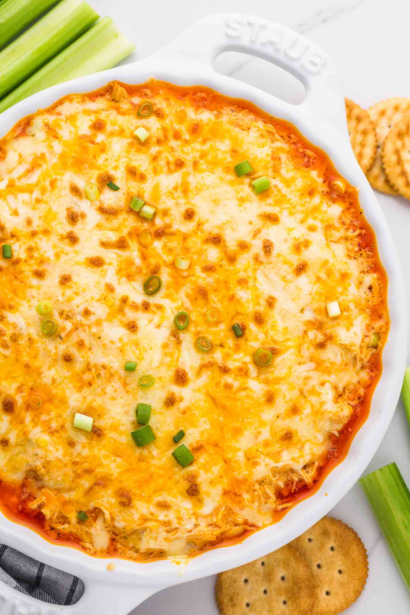 Hot buffalo chicken dip in a baking dish, with celery sticks and Ritz crackers.
