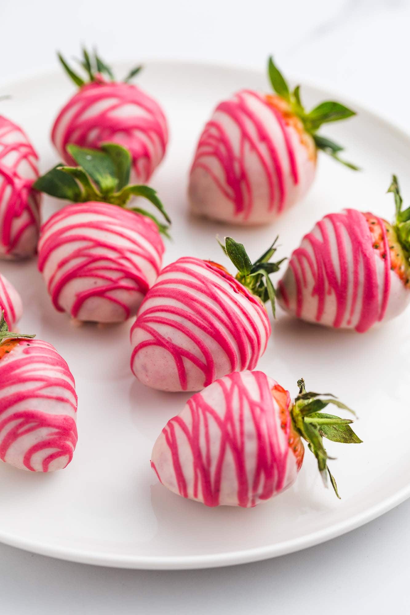 Pink chocolate covered strawberries with hot pink drizzle, on a white plate.