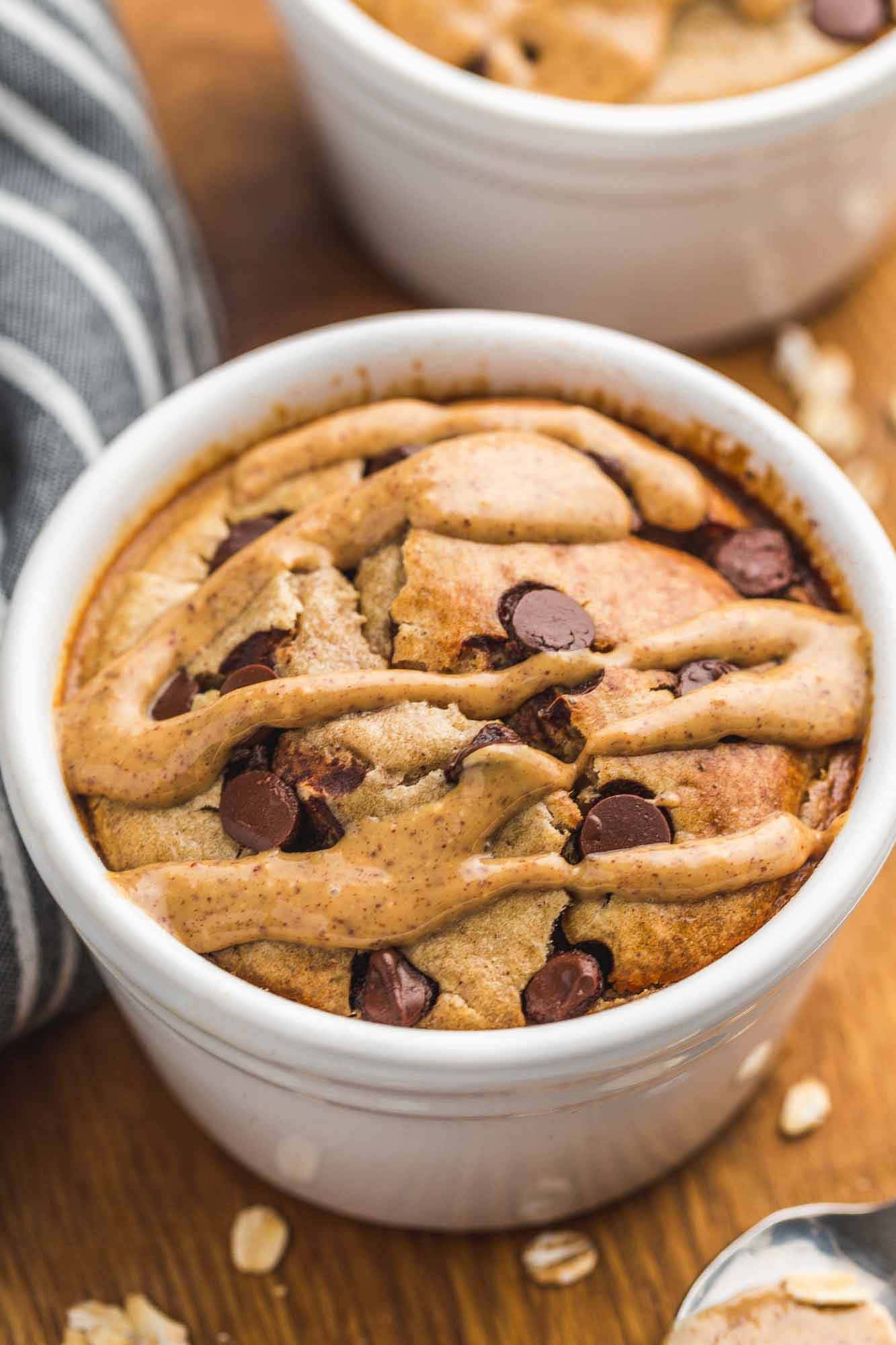 Baked Oats in white ramekin with chocolate chips, and a drizzle of peanut butter.