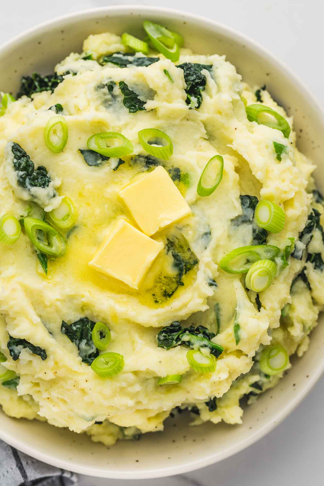Overhead shot of colcannon mashed potatoes with extra chopped green onions and knobs of butter.