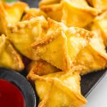 Cream cheese rangoons on a platter with sweet and sour dipping sauce