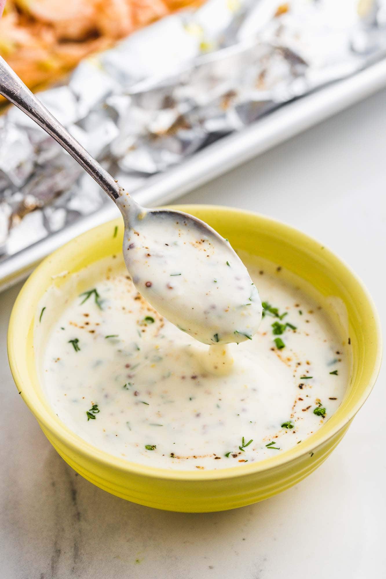 Herb cream sauce in a yellow bowl and a spoon
