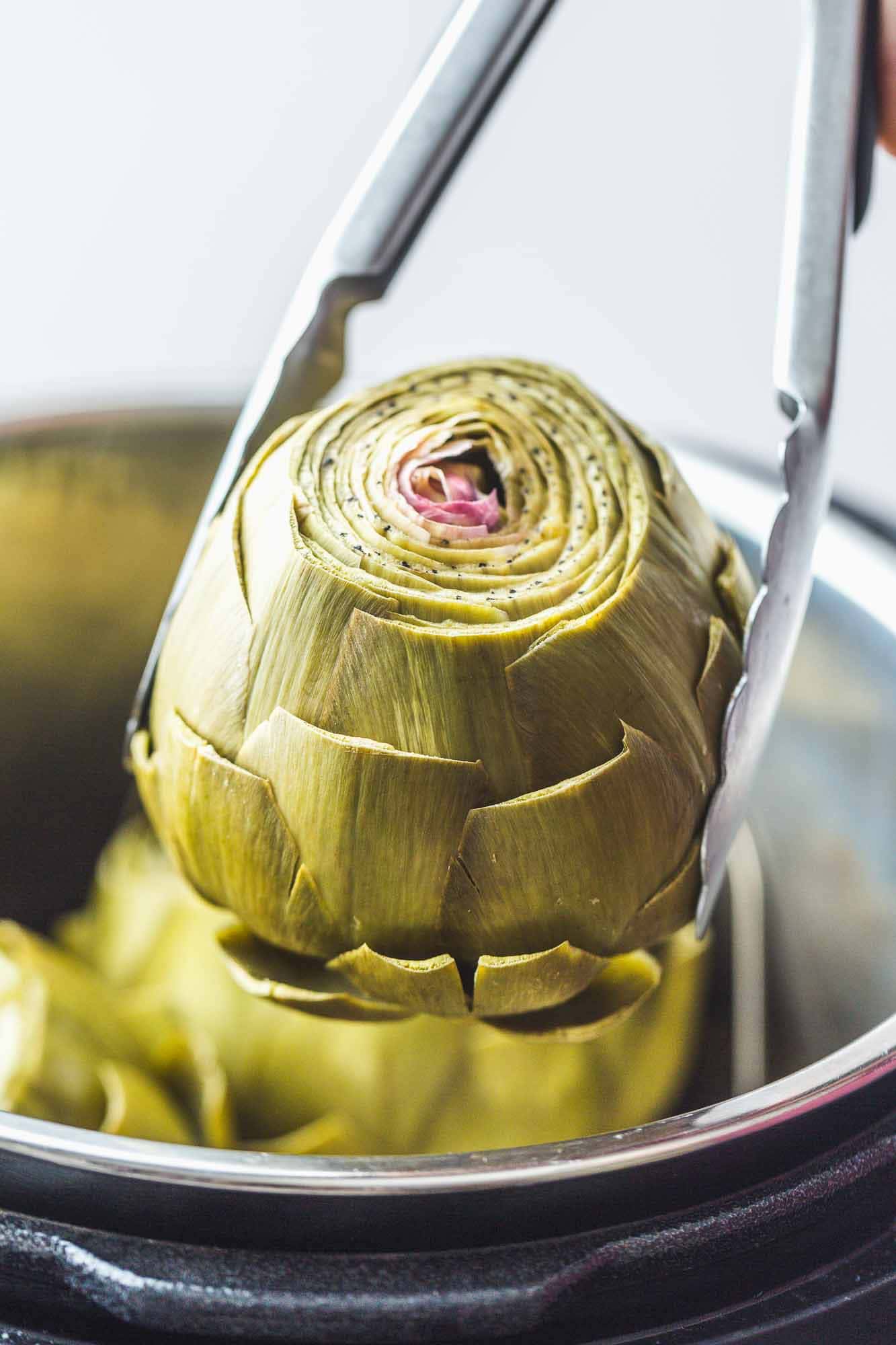 Removing pressure cooked artichokes from the Instant Pot using metal kitchen tongs.