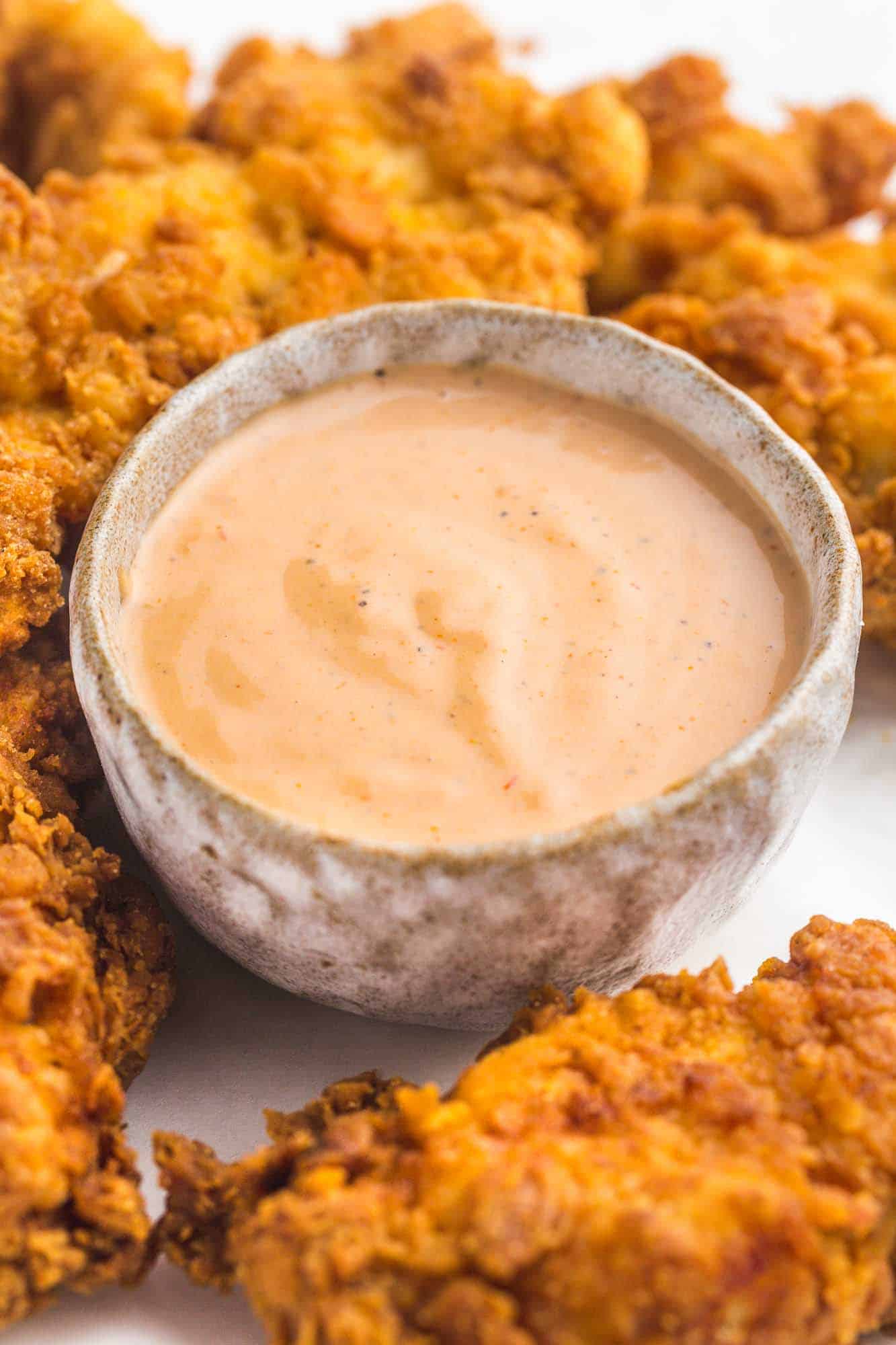 A small bowl with Cane's dipping sauce, and fried chicken tenders on the side