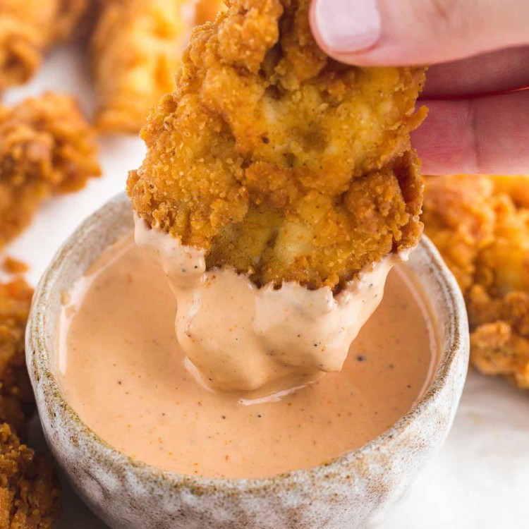 Dipping a chicken tender in Cane's Sauce
