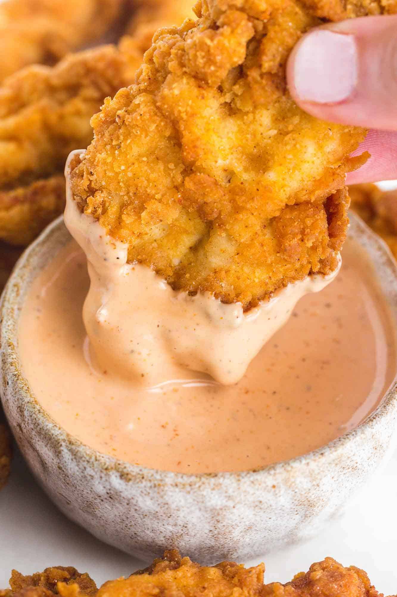 A close up of dipping a chicken tender in Cane's Sauce
