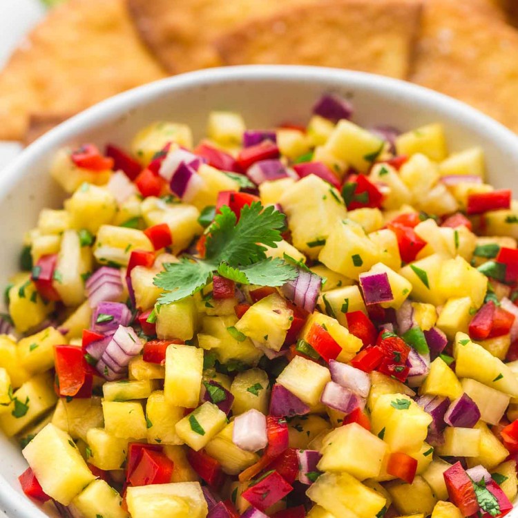 Pineapple salsa served in a white speckled bowl with tortilla chips in the background