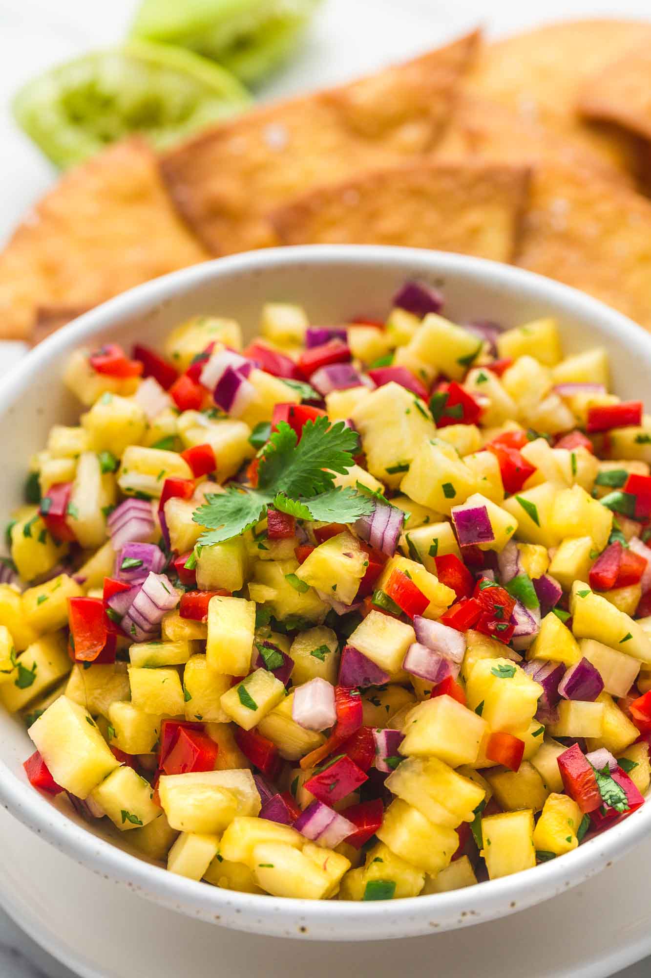 Pineapple salsa served in a white speckled bowl with tortilla chips in the background