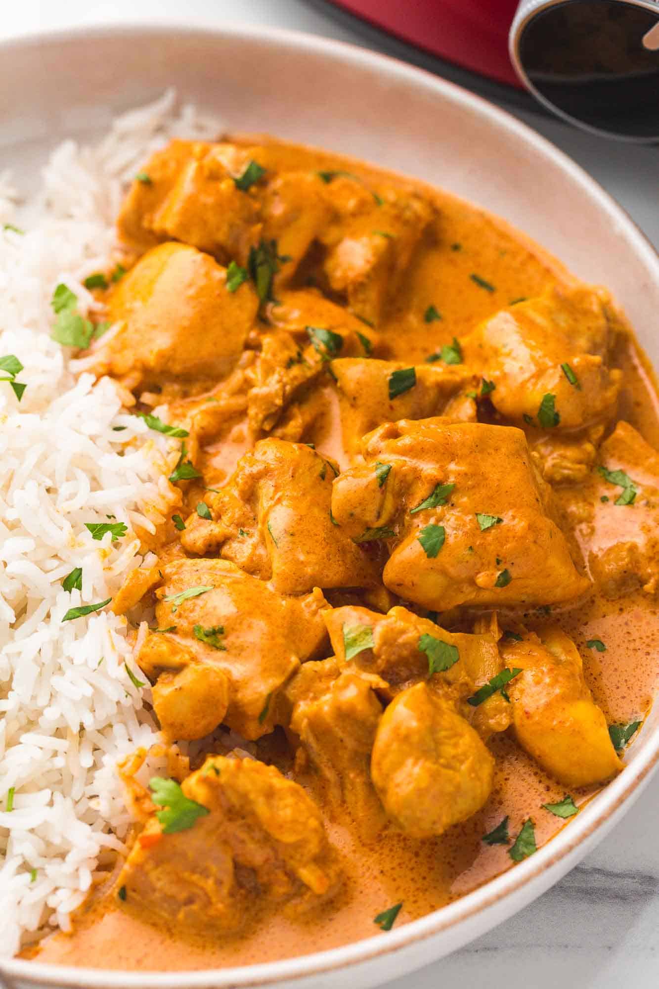 Close up shot of butter chicken served with basmati rice and a crockpot in the background