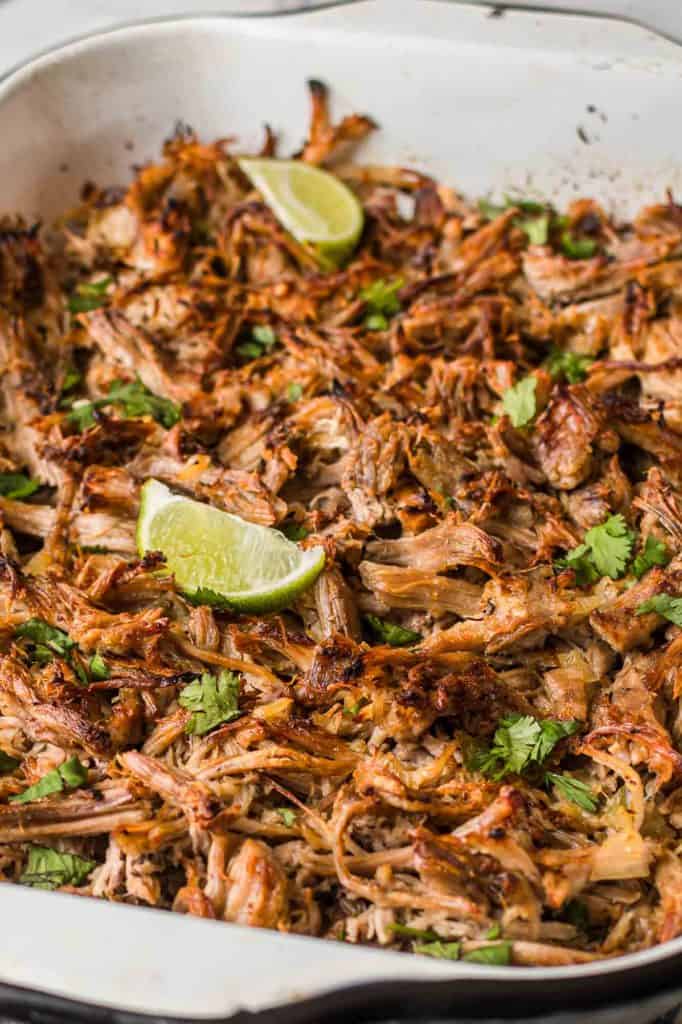 Crispy shredded carnitas in a pan with lime wedges and fresh cilantro