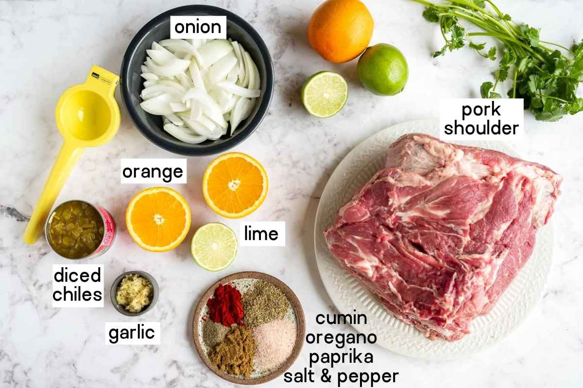 Ingredients needed to make slow cooker carnitas including pork shoulder, onion, oranges, limes, diced chiles, garlic, and seasonings.