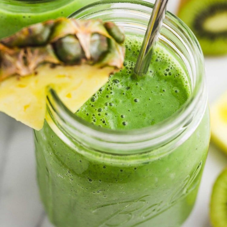 Spinach pineapple smoothie in a mason jar, served with a slice of fresh pineapple and a metal straw
