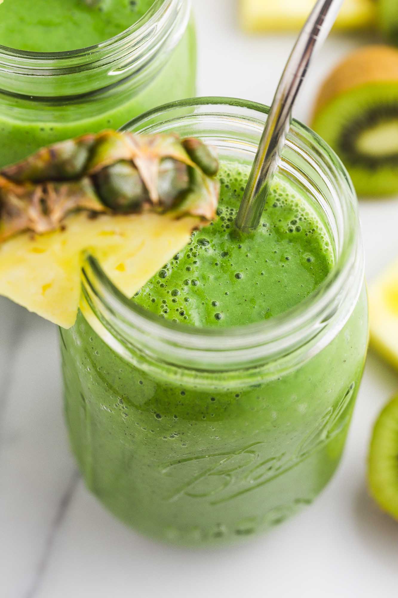Spinach pineapple smoothie in a mason jar, served with a slice of fresh pineapple and a metal straw