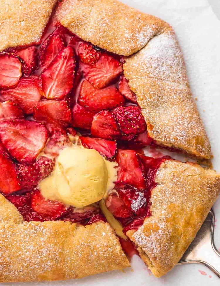 Overhead shot of a strawberry galette sprinkled with powdered sugar and topped with vanilla ice cream