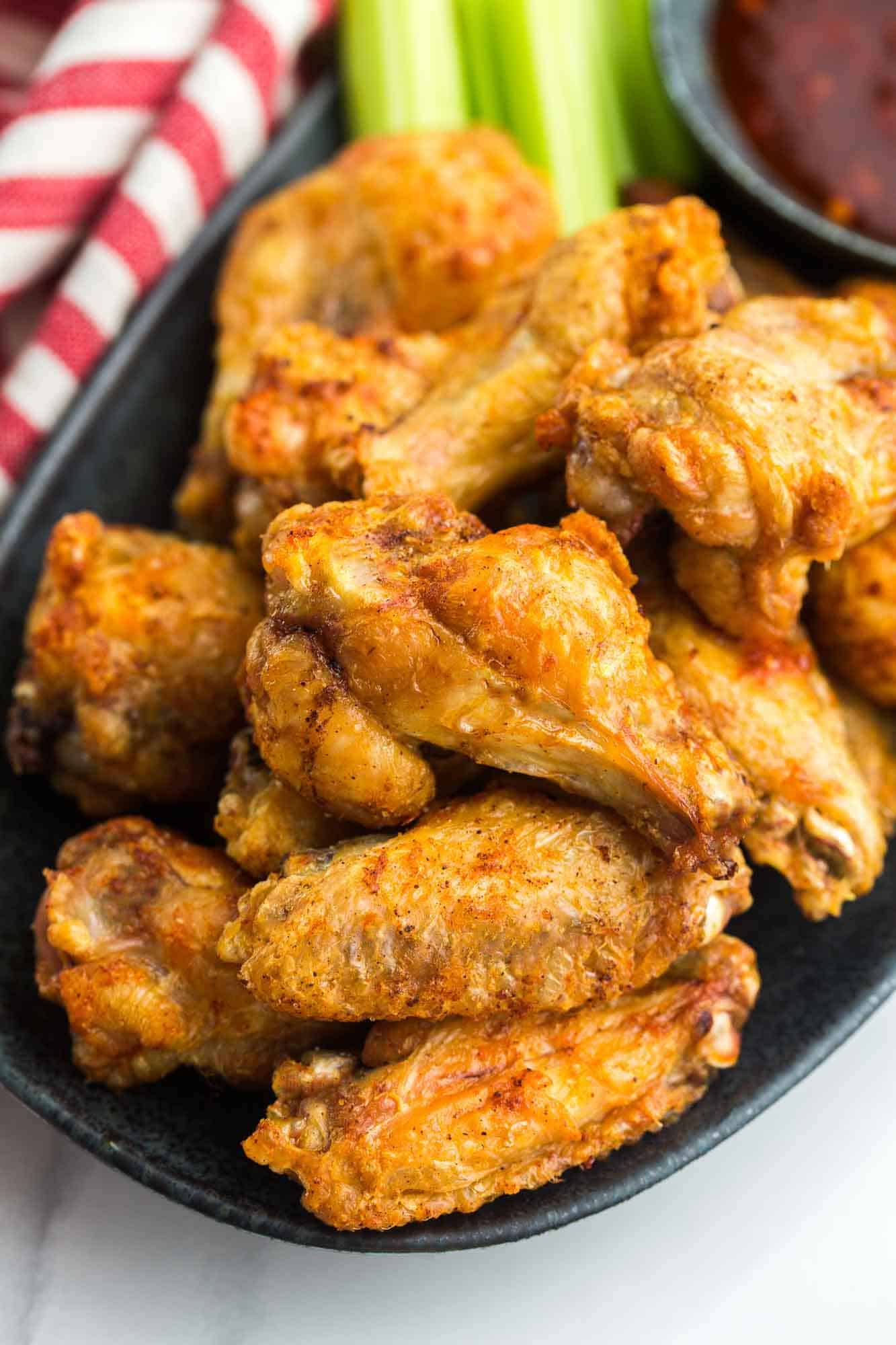 Crispy chicken wings on a black platter with celery sticks