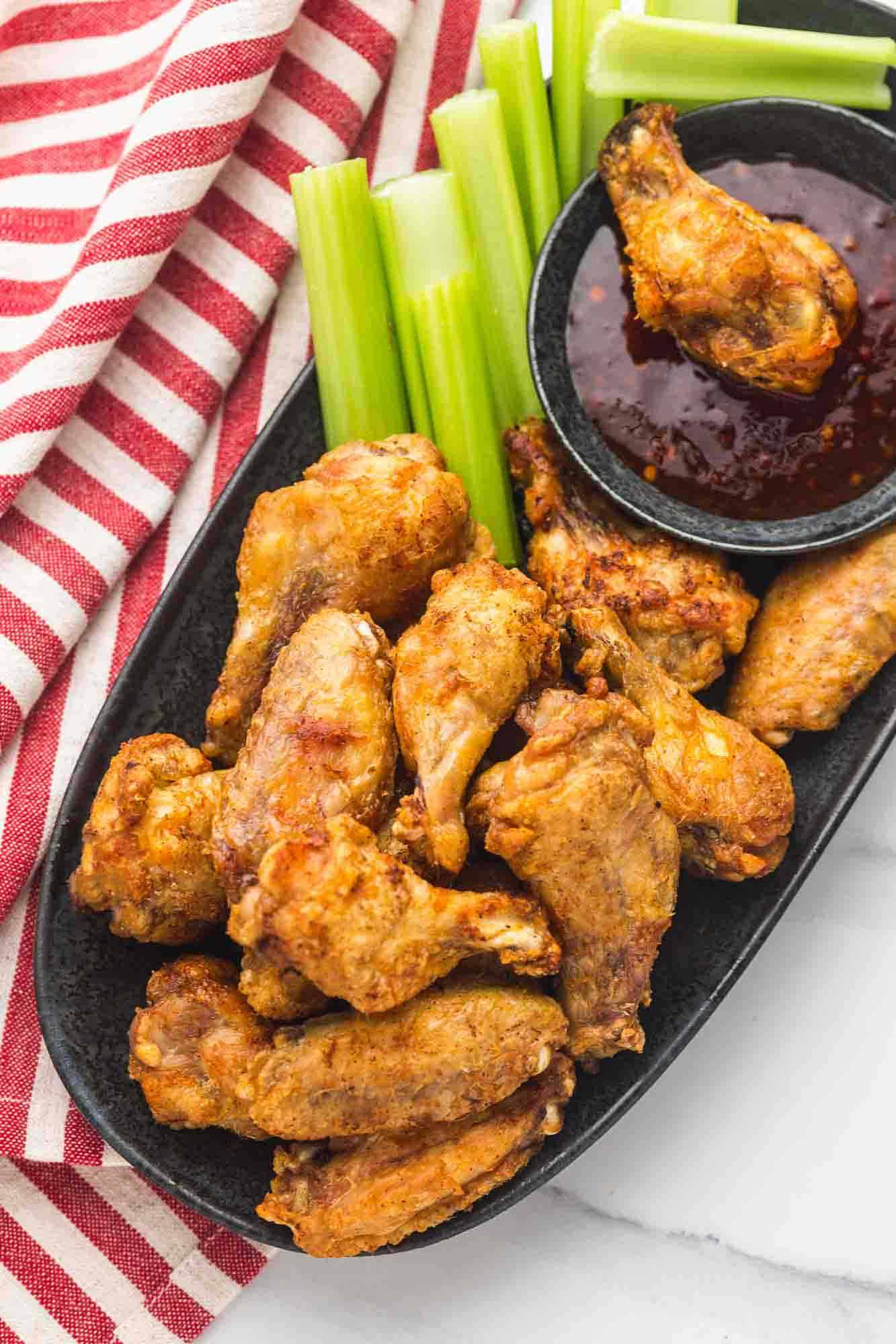 chicken wings on a black platter with sweet chili sauce and celery sticks