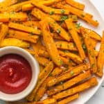 Sweet potato fries on a white plate with tomato sauce on the side