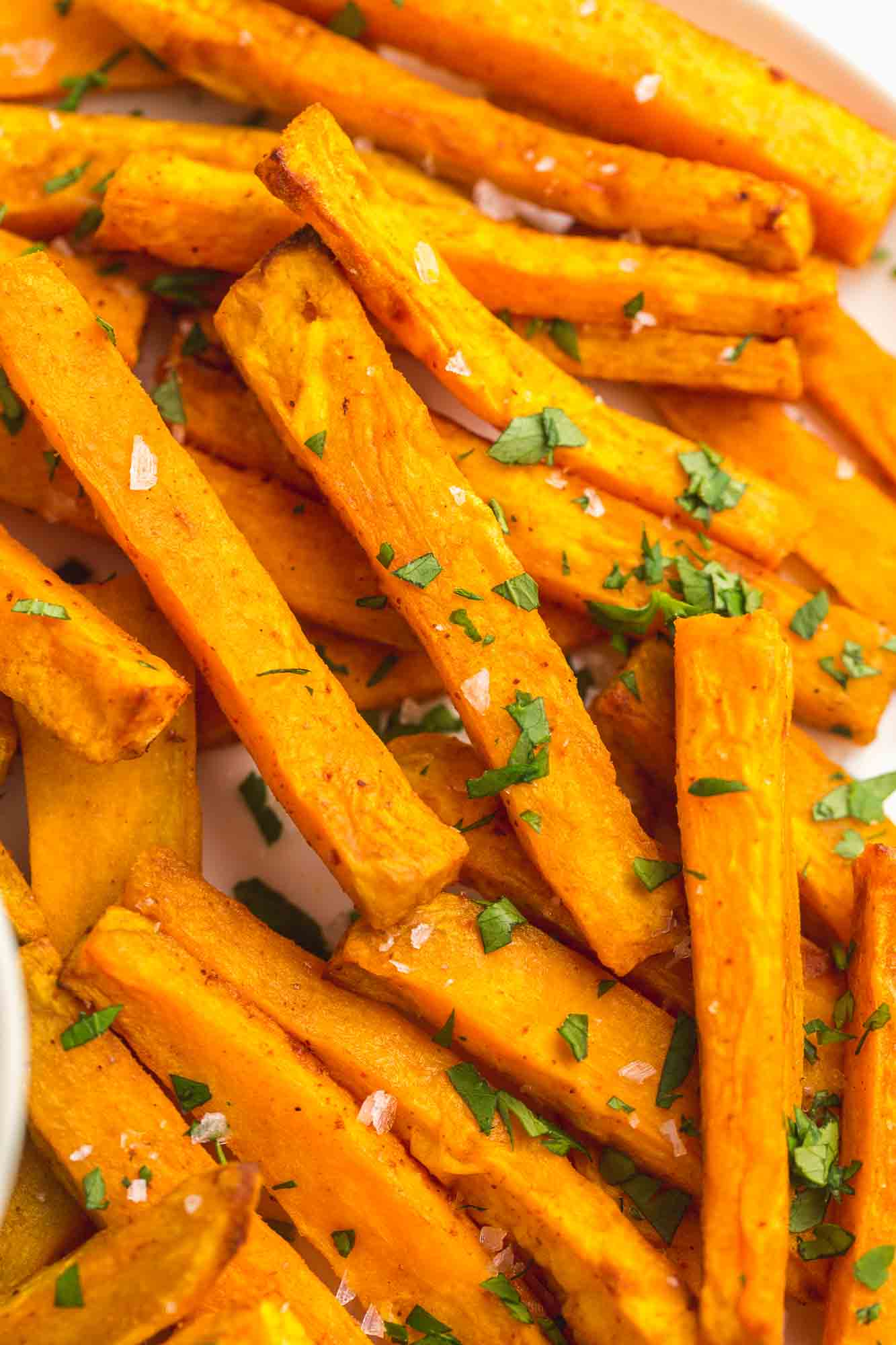 Close up shot of sweet potato fries garnished with chopped parsley and sea salt flakes