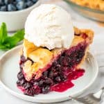 A slice of blueberry pie served on a small white plate with vanilla ice cream