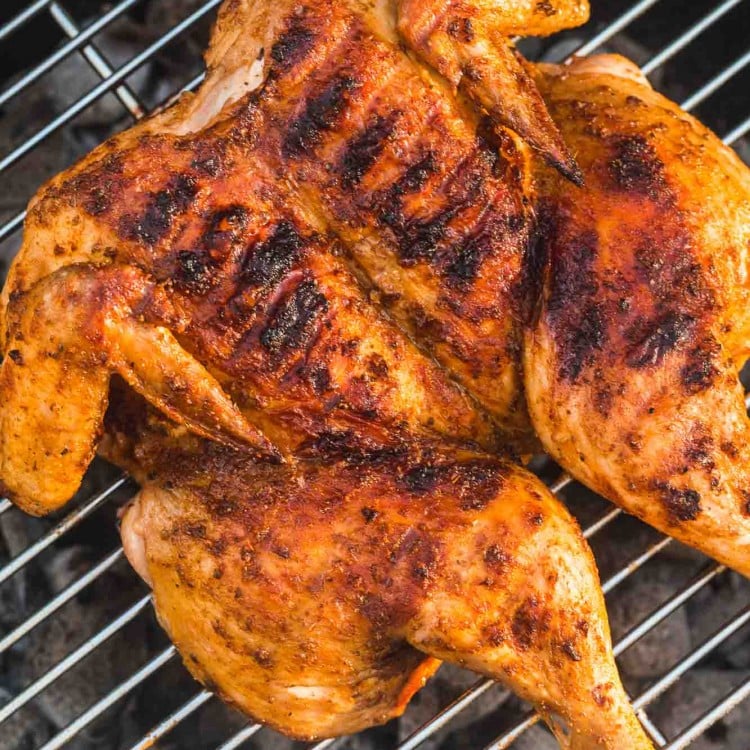 Spatchcocked grilled chicken placed on a coal grill