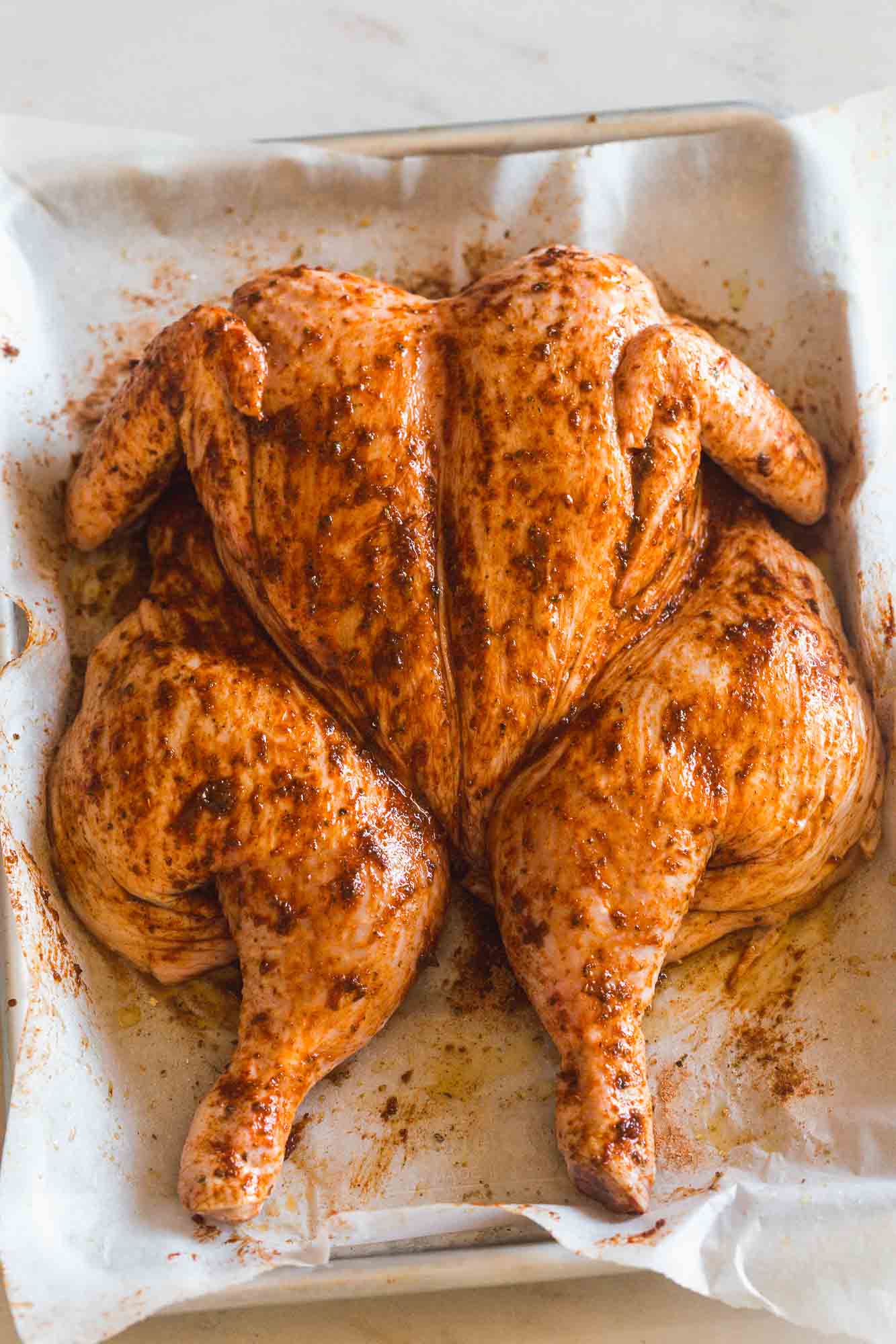 Raw spatchcocked whole chicken seasoned and placed on a sheet pan lined with parchment paper