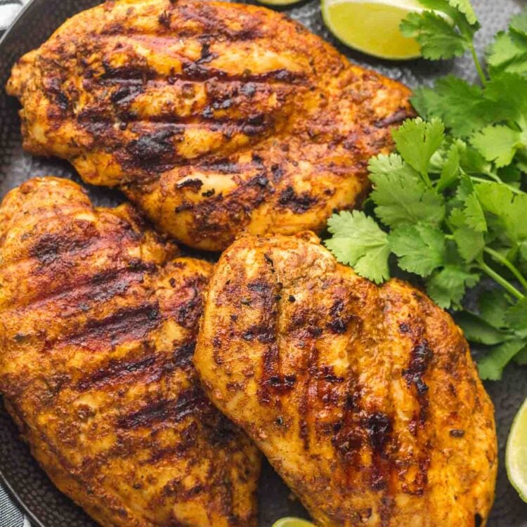 Grilled Mexican marinated chicken served on a large black plate with fresh cilantro and lime wedges