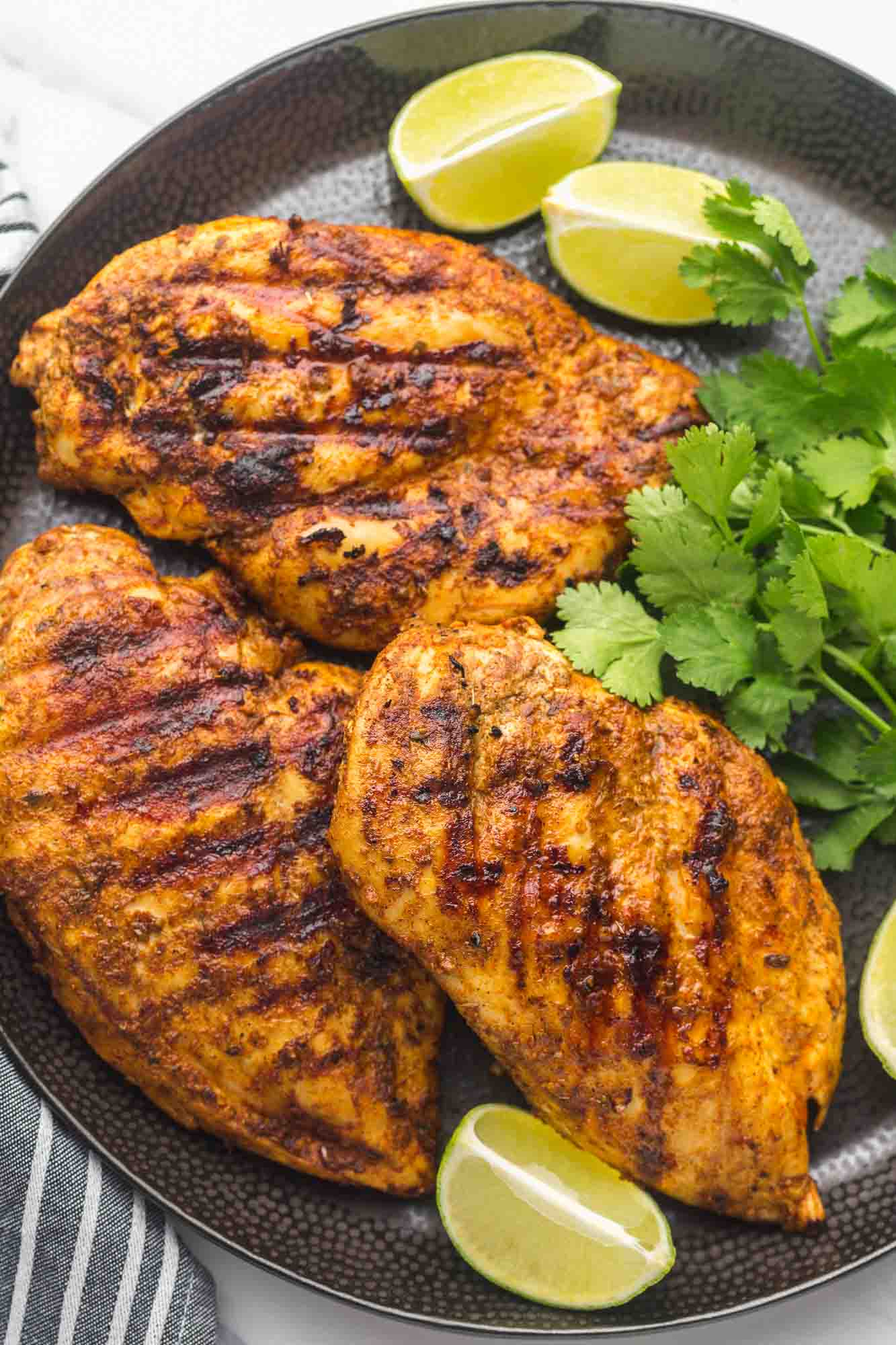 Grilled Mexican marinated chicken served on a large black plate with fresh cilantro and lime wedges