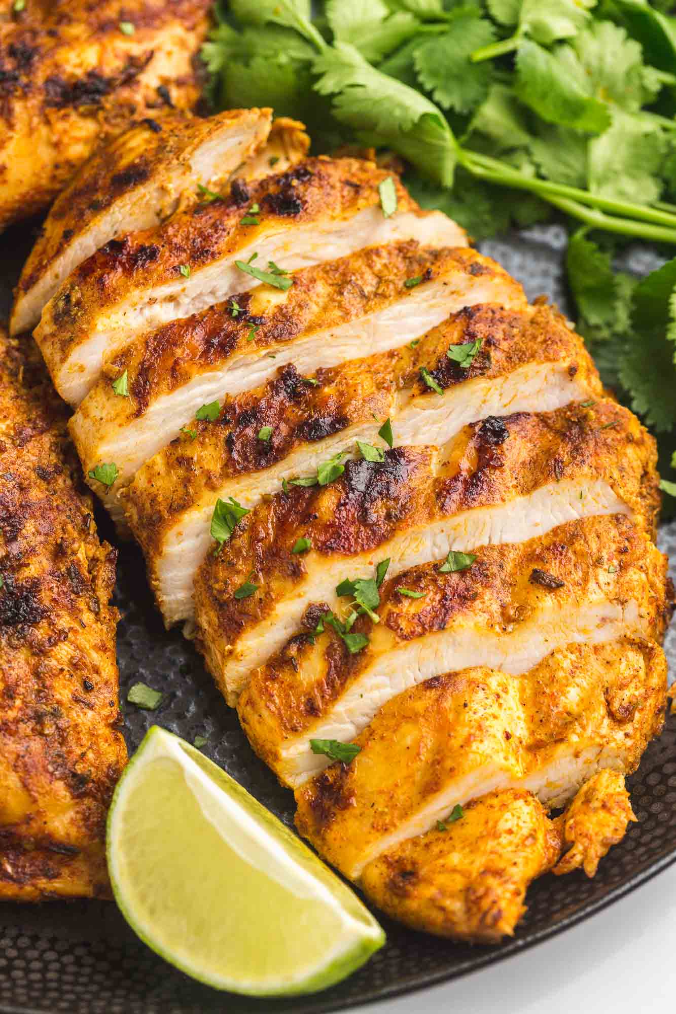 Grilled and sliced chicken breast served on a black plate with fresh lime wedge and fresh cilantro leaves