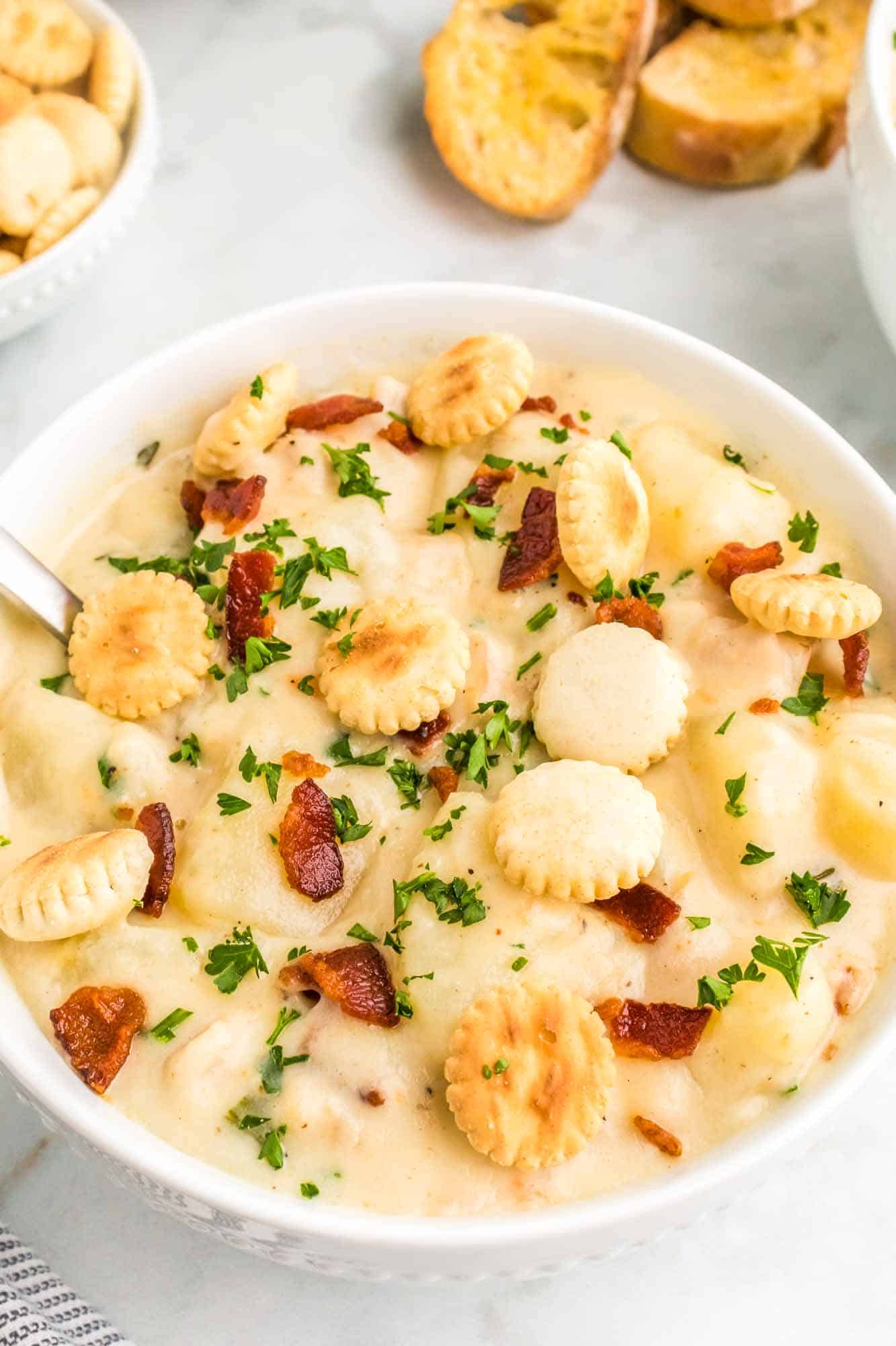 Creamy clam chowder served in a white bowl, topped with extra crispy bacon and oyster crackers.
