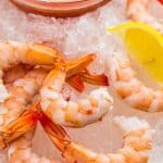 Close up shot of poached shrimp served over crushed ice with lemon wedges and shrimp cocktail on the side