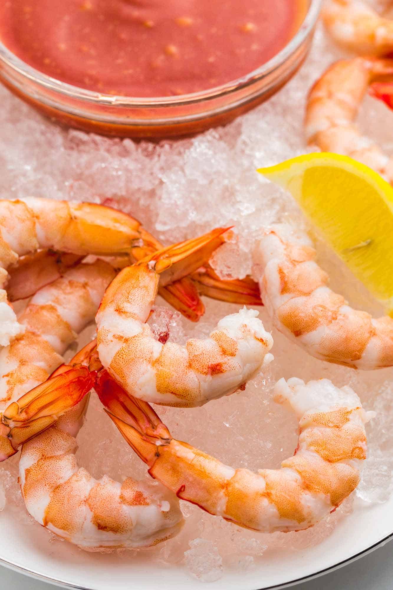 Close up shot of poached shrimp served over crushed ice with lemon wedges and shrimp cocktail on the side