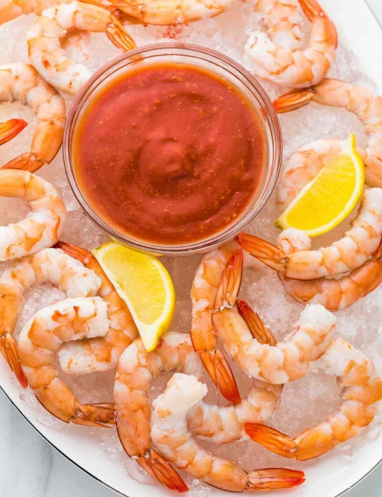Poached shrimp served over ice on a white platter with lemon wedges and Cocktail sauce