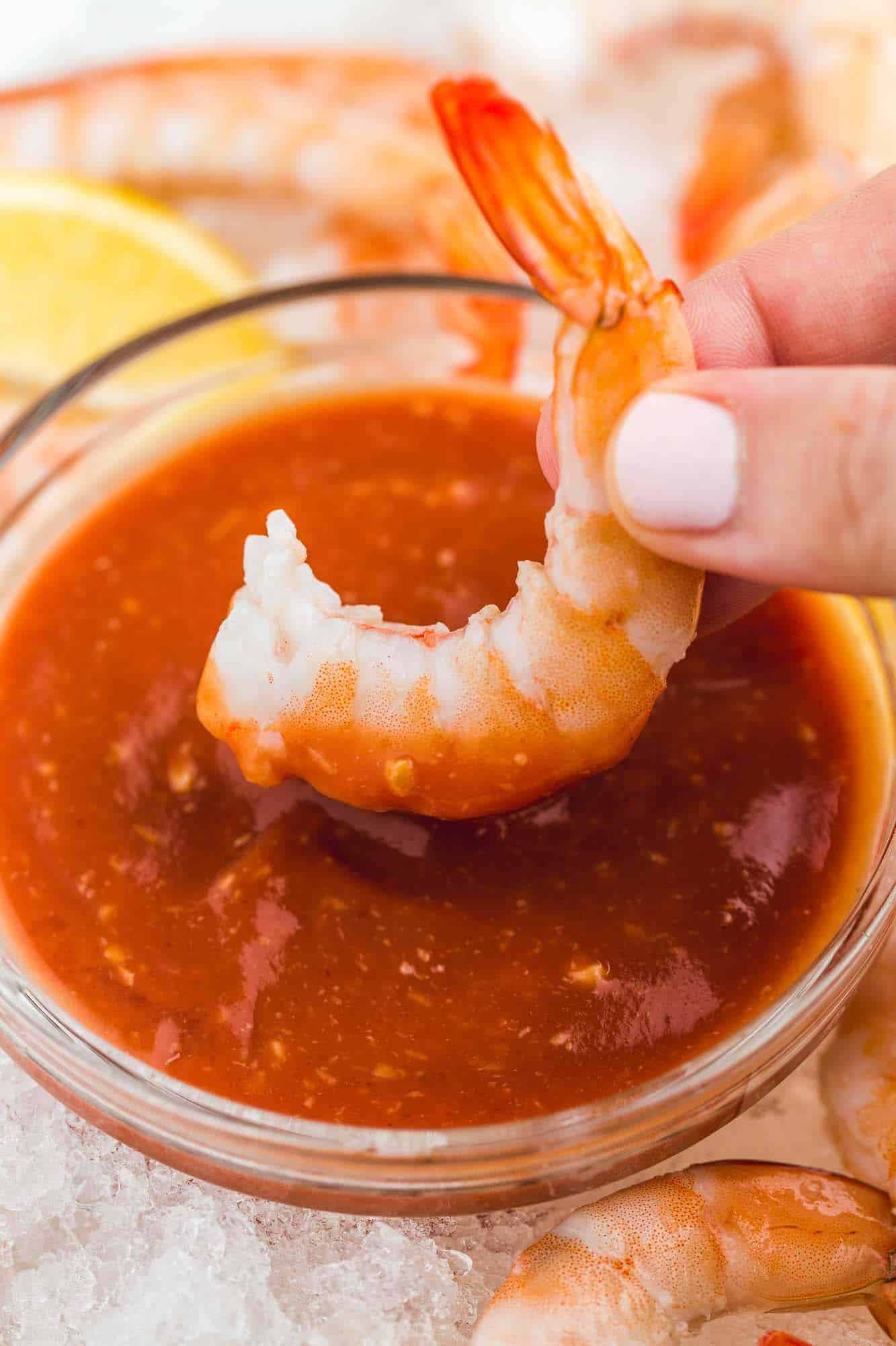 Dipping a cooked jumbo shrimp in cocktail sauce that's served in a small glass bowl