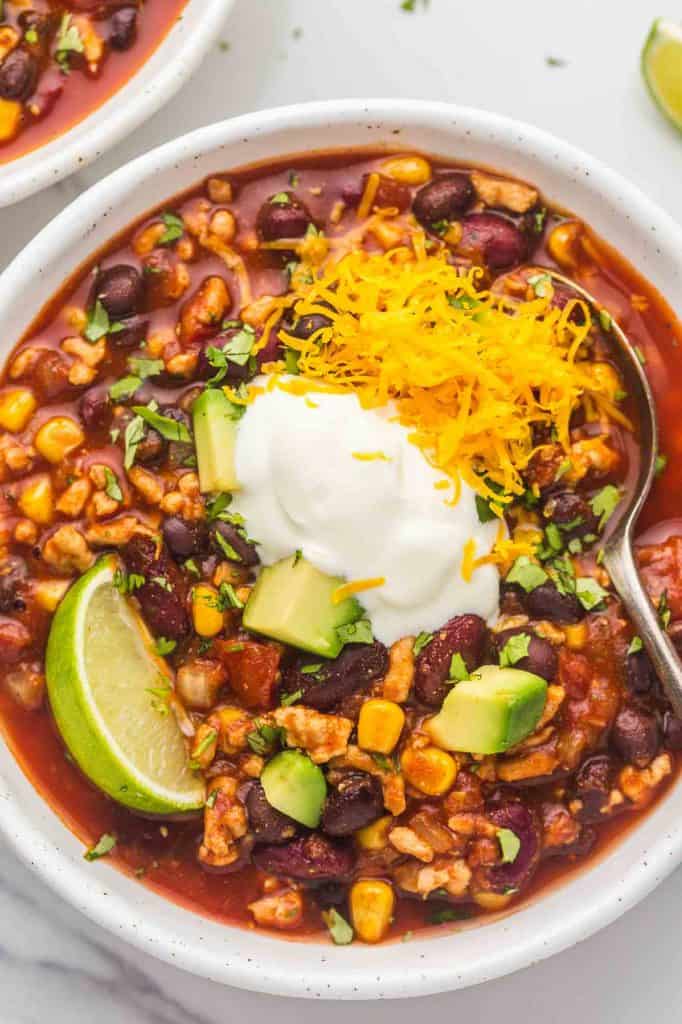 An overhead shot of a bowl with turkey chili and toppings like lime wedge, sour cream, diced avocado, and cheese