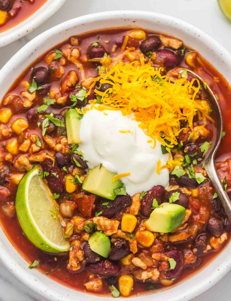 An overhead shot of a bowl with turkey chili and toppings like lime wedge, sour cream, diced avocado, and cheese