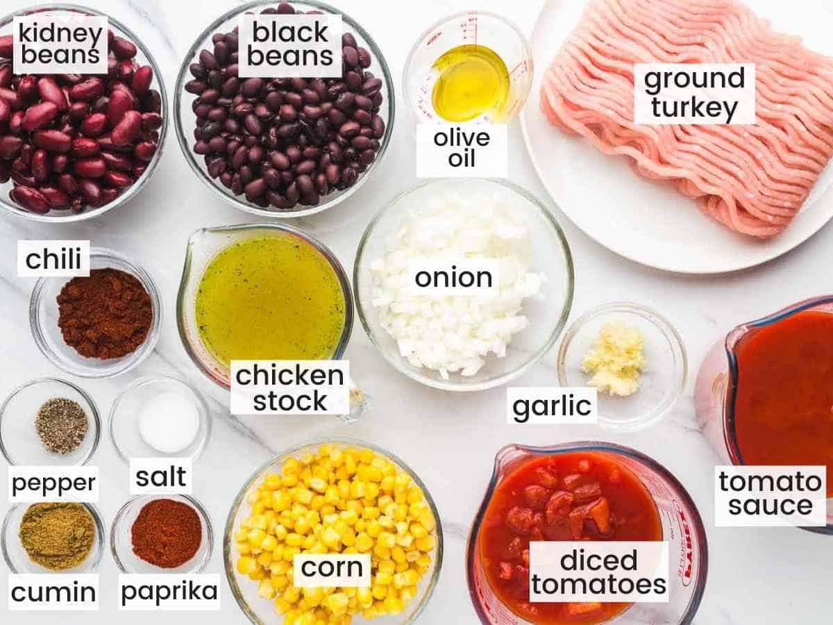 Ingredients needed to make turkey chili including ground turkey, corn, kidney and black beans, tomato, onion, garlic, chicken stock, and spices.