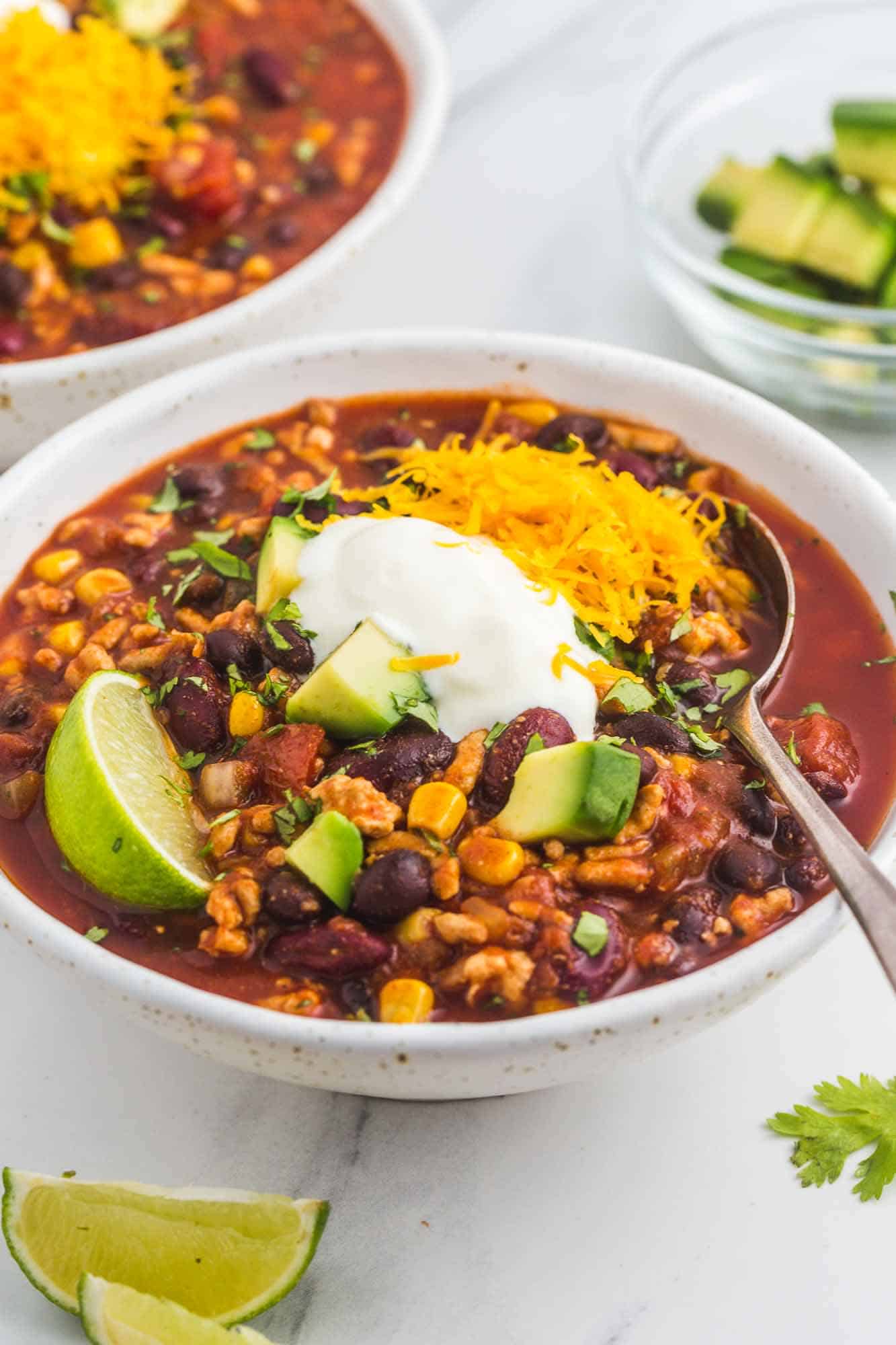 Turkey chili in 2 speckled white bowls with toppings