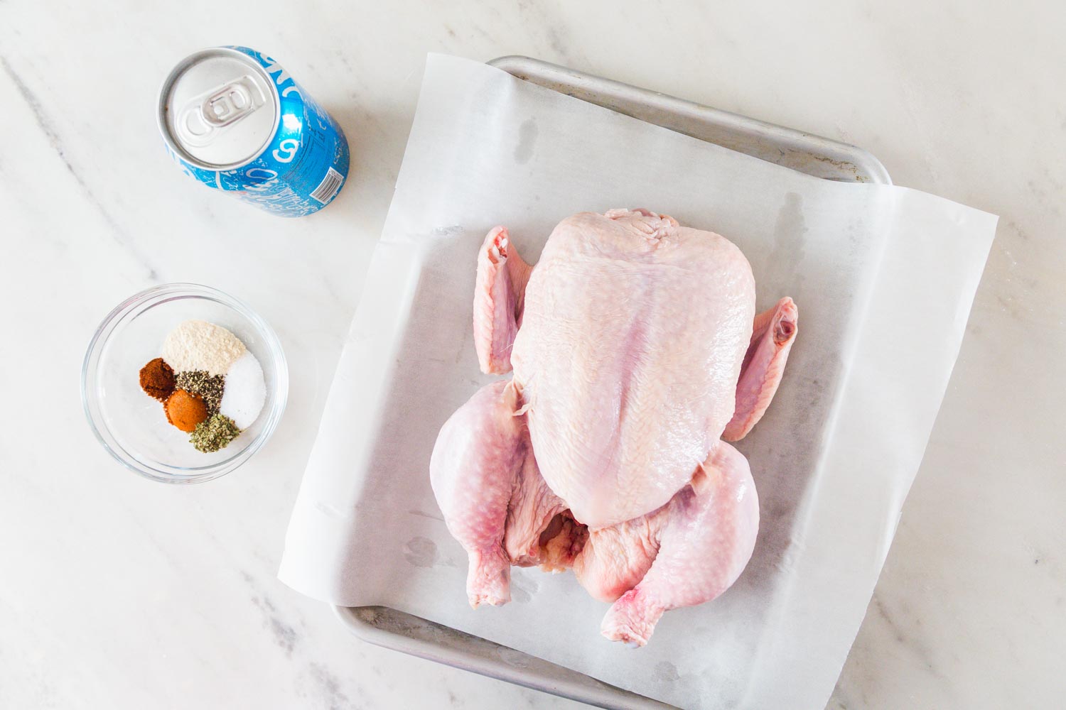 Ingredients needed to make beer can chicken including a raw whole chicken, a beer, and spice rub