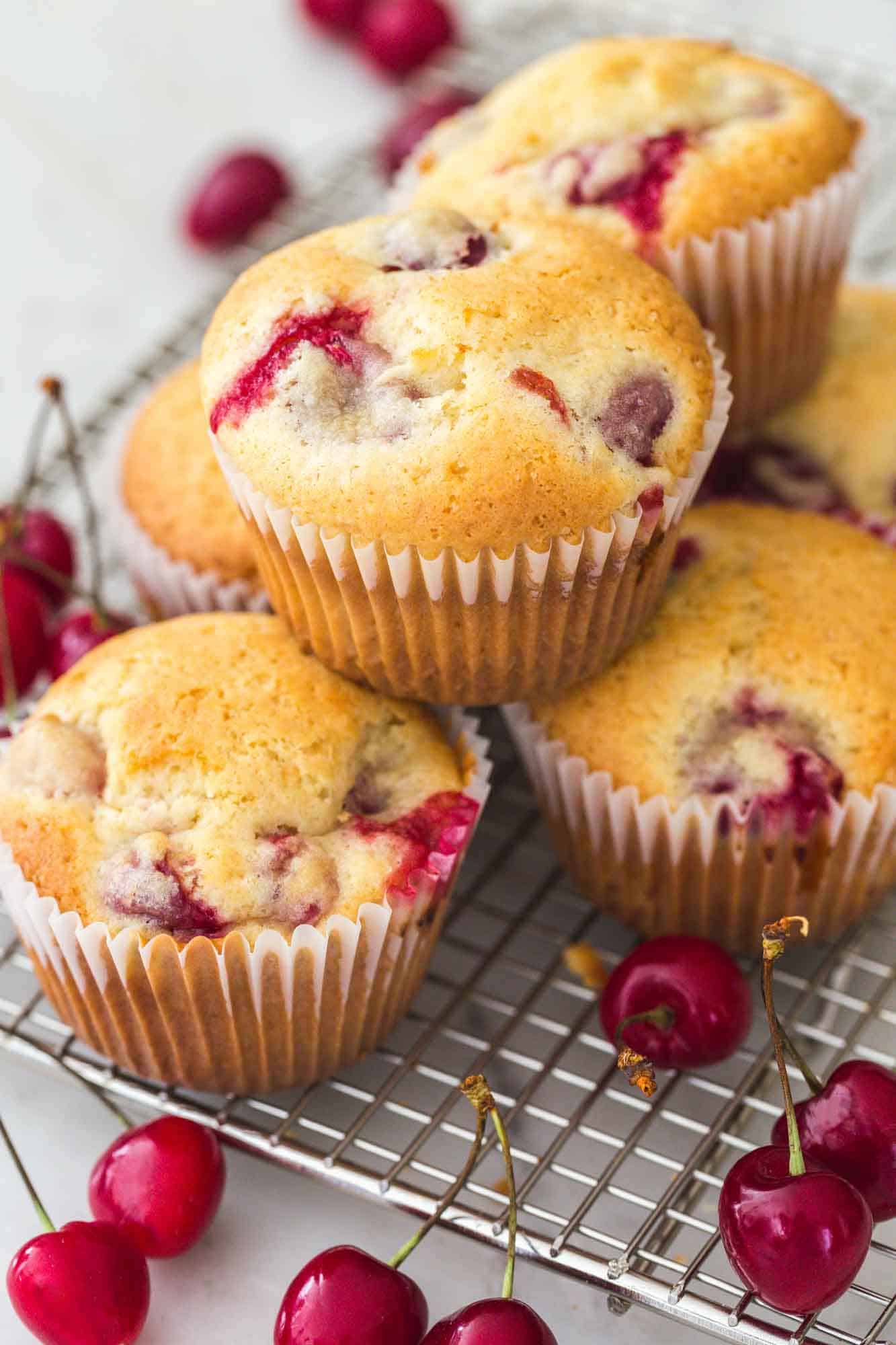Cherry muffins placed and stacked on a wire rack with fresh cherries on the sides