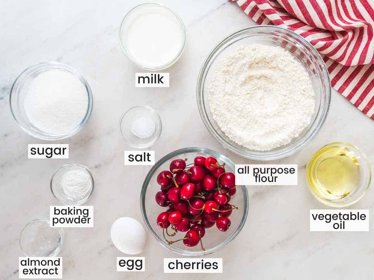 Ingredients needed to make cherry muffins including cherries, flour, oil, baking powder, salt, sugar, egg, and milk.