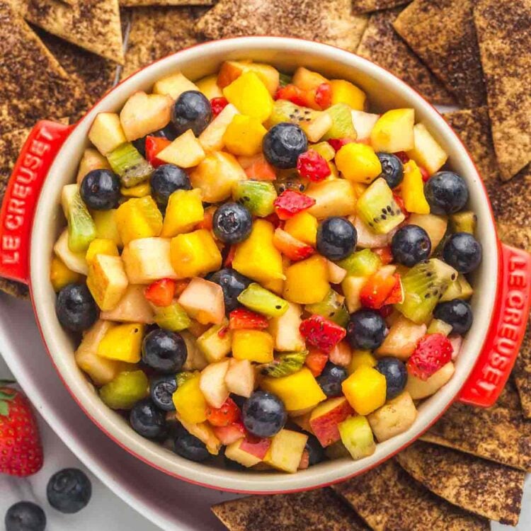 Fruit salsa served in a red Le Creuset dish, with crunchy cinnamon chips on the sides served in a large white platter.