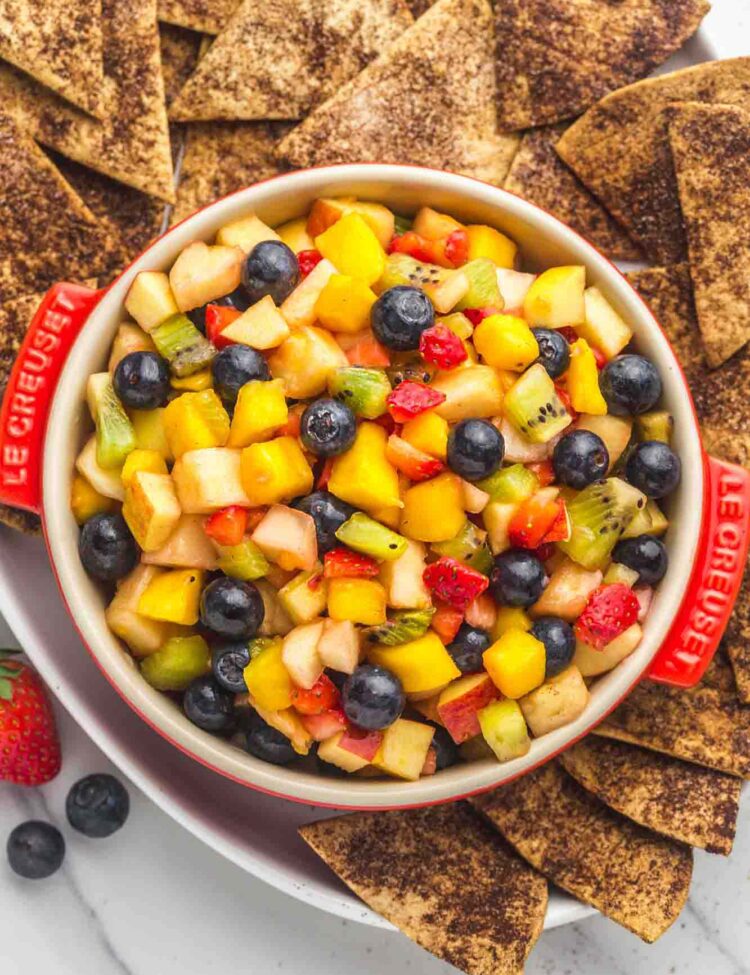 Fruit salsa served in a red Le Creuset dish, with crunchy cinnamon chips on the sides served in a large white platter.