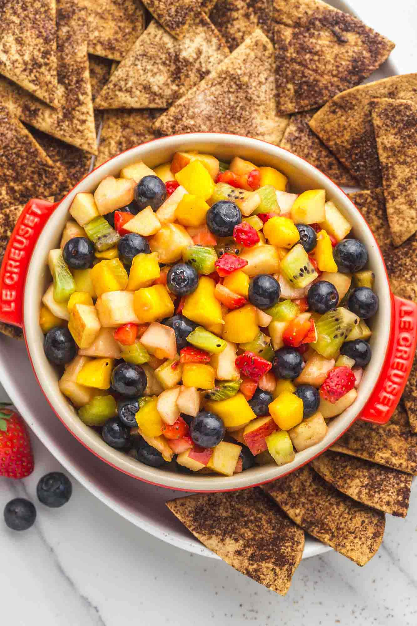 Fruit salsa served in a red Le Creuset dish, with crunchy cinnamon chips on the sides served in a large white platter.