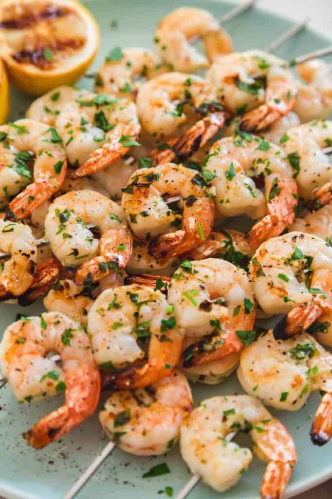 Grilled shrimp skewers served on a blue platter with grilled lemons, and chopped parsley
