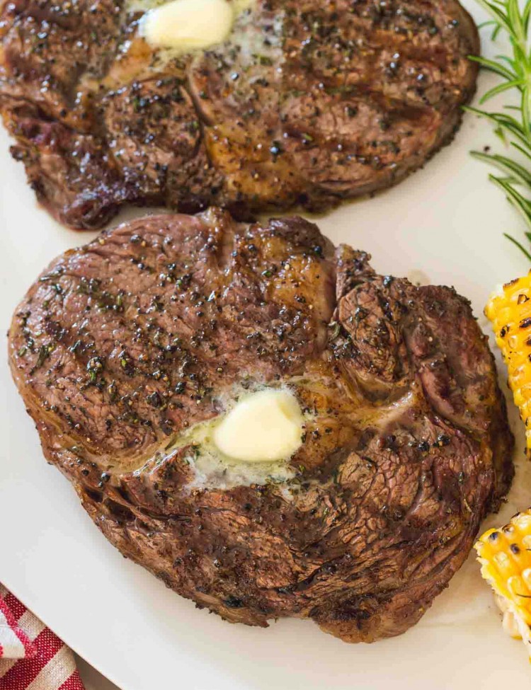 2 grilled steaks on a white plate with melted butter
